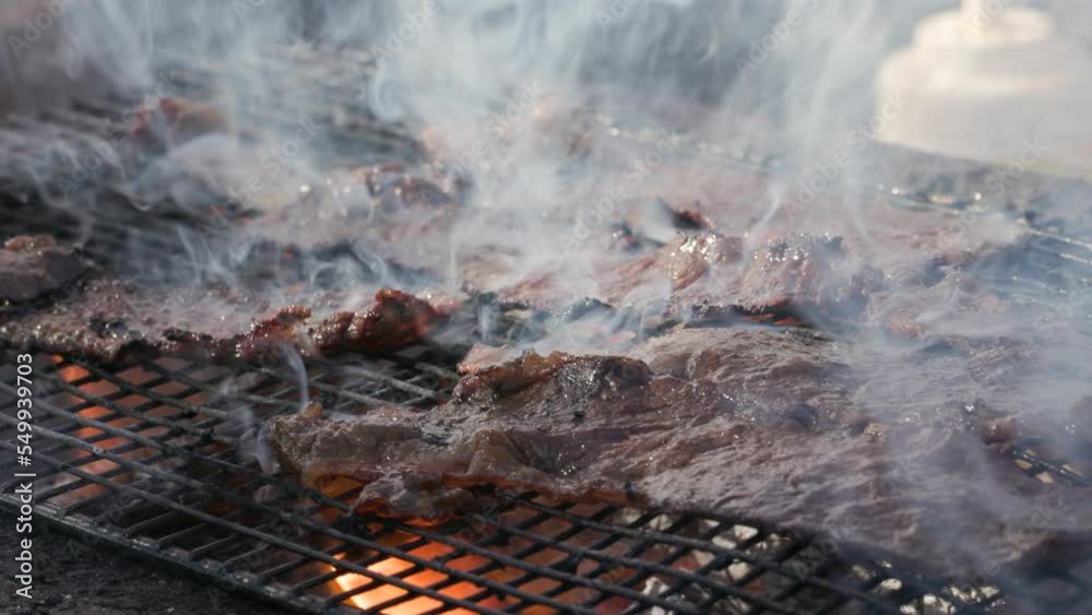 Detailed view of raw, fresh red meat on a grill covered with whitish steam. Close-up shot of traditional, grilled steaks and bacon cooking outdoors. High quality 4k footage Detailed view of raw, fresh red meat on a grill covered with whitish steam. Close-up shot of traditional, grilled steaks and bacon cooking outdoors. High quality 4k footage