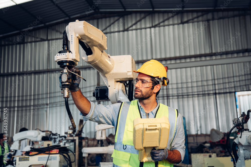 Male engineers or worker is controlling robot arm machine welding steel, worker using forcing welding with a control screen which is used for precision welding control. Male engineers or worker is controlling robot arm machine welding steel, worker using forcing welding with a control screen which is used for precision welding control.
