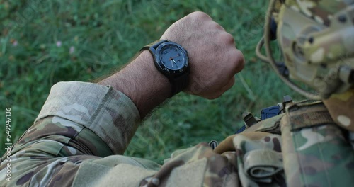 Close-up unrecognizable male soldier in camouflage uniforms getting ready for military exercises or battle. Detailed shot of military man checking time, looking at watch. Ukrainian russian war