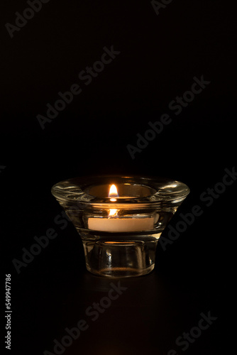 Glass candlestick with a burning candle isolated on a black background. Concept of memorial day, holiday, blackout, darkness, light. Place for text.