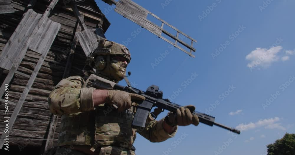 Close up unrecognizable armed soldier in a camouflage uniform standing near a large wooden windmill, World food crisis, war, grain agreement, Ukraine Close up unrecognizable armed soldier in a camouflage uniform standing near a large wooden windmill, World food crisis, war, grain agreement, Ukraine