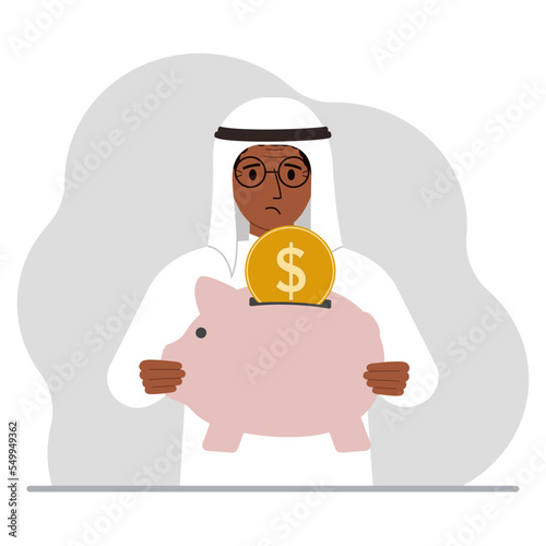Sad muslim man holds a piggy bank, a coin falls into the piggy bank. The concept of saving finance, savings, investing finances.