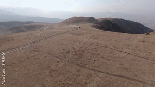 SUV car speed race riding towards on dirt road at desert sand mountain with blue sky aerial view. FPV sports drone shot extreme dust automobile drive journey transportation offroad rally tourism 4k