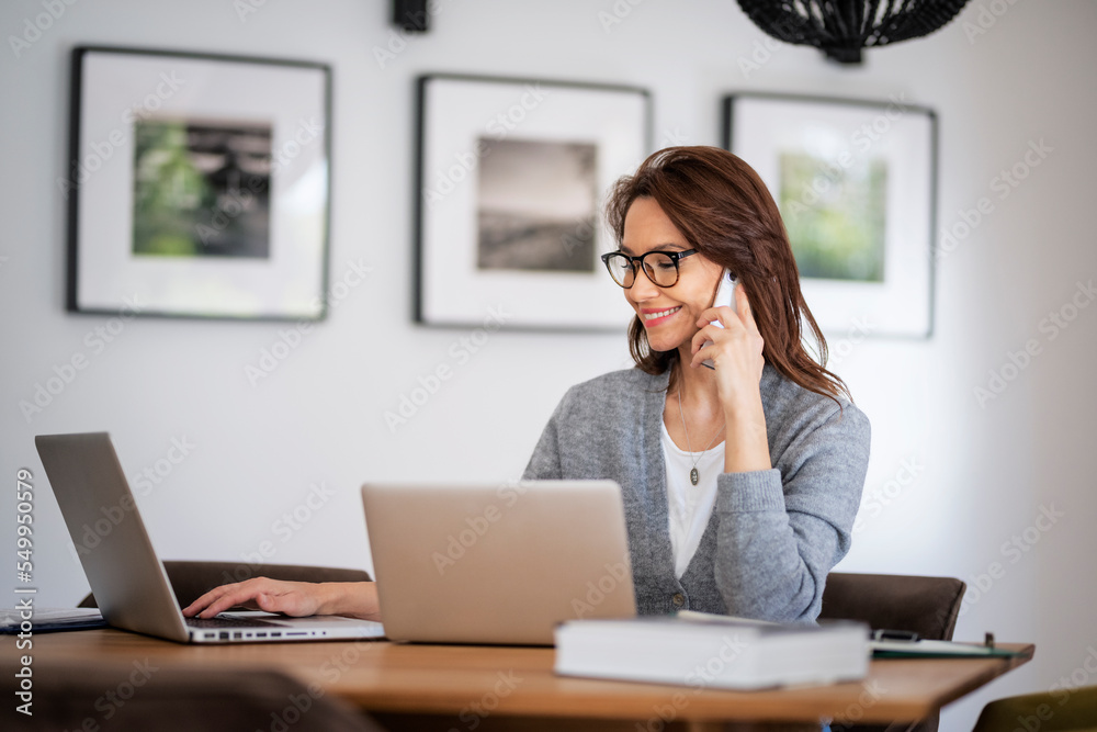 Business woman using mobile phone in front of laptops while working from home Business woman using mobile phone in front of laptops while working from home