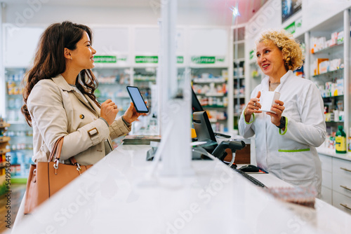 Obraz na plátně Woman looking for medicine with mobile phone at pharmacy.