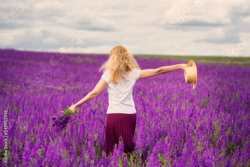 Fototapeta Naklejka Na Ścianę i Meble -  A girl running across a flowering field with a bouquet of lilac flowers 