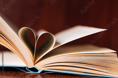 Open book, heart shape on wooden table