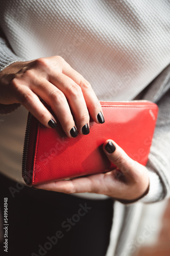 Beautiful black painted nails on woman's hand holding a red wallet. Winter manicure. © Robert Petrovic