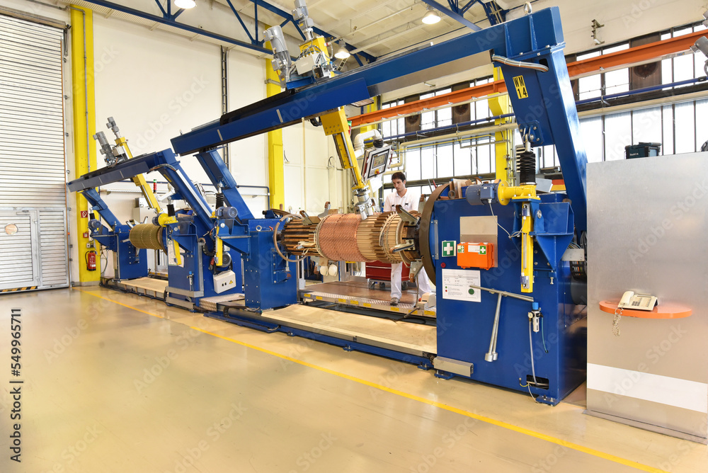 young mechanical engineering workers operate a machine for winding copper wire - manufacture of transformers in a factory