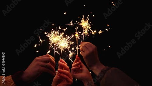 Hands of people with sparklers celebrating new year holiday at night. Beautiful bokeh lights background. New Year party, holiday concept