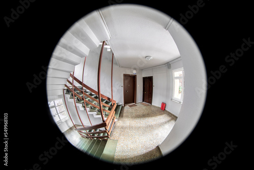 Empty corridor, floor, stairways and two neighboring doors are visible through the door peephole        photo