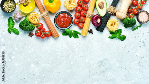 Assortment of dry colorful spaghetti and pasta with cherry tomatoes and ingredients, on a gray stone background. Dry pasta. Top view. Free space for text.