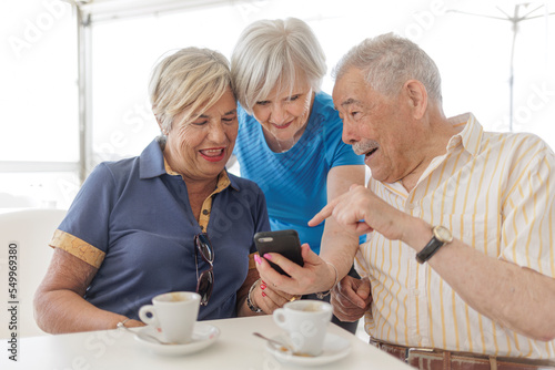 gruppo di tre anziani sorridenti guarda il cellulare seduti comodamente in un tavolino
