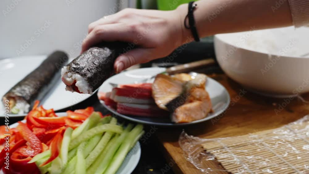 Person Holding Green Sushi Roll To Place It In White Plate, Homemade Preparation Person Holding Green Sushi Roll To Place It In White Plate, Homemade Preparation