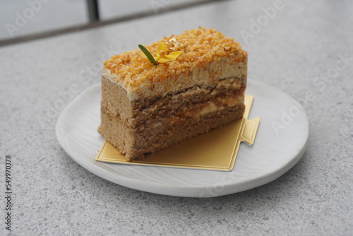 coffee almond crunchy cake on gold paper on white ceramic plate  on grey marble background  dessert  food  snack  copy space