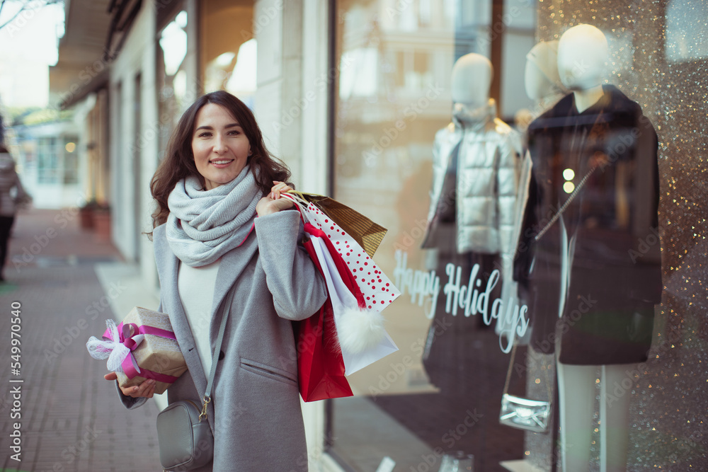 Young happy smiling woman holding shopping bags and Christmas presents in her hands. Concept of European winter holidays, sales and gifts, or black friday.
