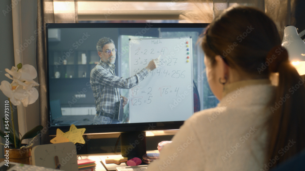 Young asian girl sits at the table at cozy room and learns new material. Schoolgirl listens online lesson of math and studies on pc. Mature teacher talks with student and shows equation on board Young asian girl sits at the table at cozy room and learns new material. Schoolgirl listens online lesson of math and studies on pc. Mature teacher talks with student and shows equation on board