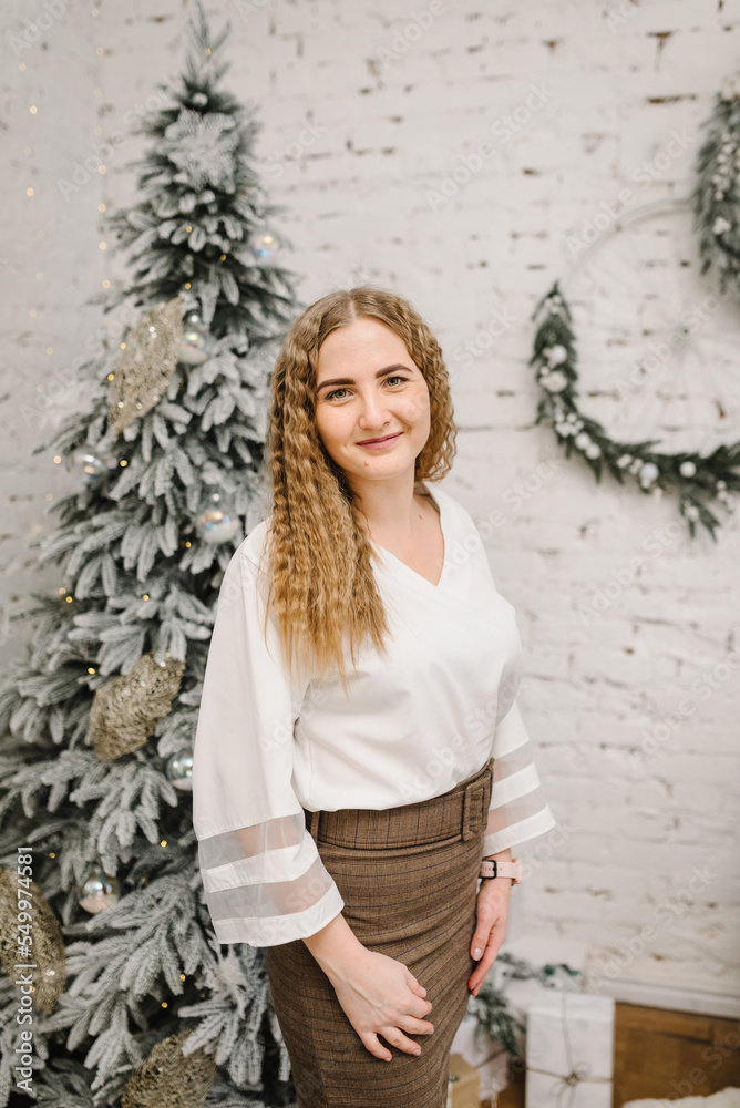 A beautiful young girl is standing near Christmas tree in living room. Christmas tree and home decorated interior. Happy New Year. Fashion woman relaxing in the warm and cozy evening at home. Closeup. A beautiful young girl is standing near Christmas tree in living room. Christmas tree and home decorated interior. Happy New Year. Fashion woman relaxing in the warm and cozy evening at home. Closeup.