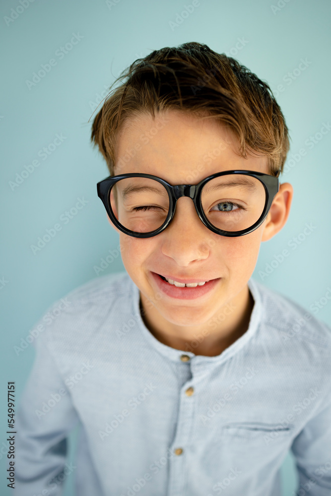 young cool boy with blue shirt, with big massive black glasses standing in front of blue background