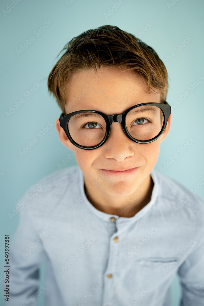 young cool boy with blue shirt, with big massive black glasses standing in front of blue background