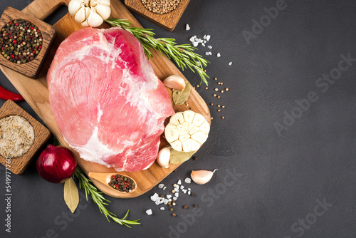 View above raw boneless pork shoulder ready for roasting with seasoning over dark concrete background with copy space. Organic meat for main dish