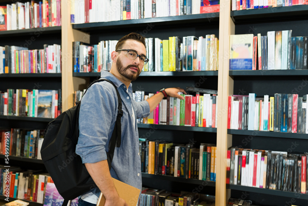 Caucasian man at the bookstore looking at the camera while choosing a book Caucasian man at the bookstore looking at the camera while choosing a book