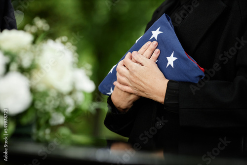 Woman holding American flag to chest at outdoor funeral ceremony for veteran, closeup