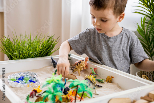 Cute baby boy playing sensory box kinetic sand table with carnivorous and herbivorous dinosaurs photo