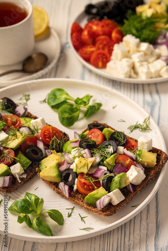 Tasty and healthy avocado, olives, cherry tomatoes and feta cheese sandwiches. Toasts with avocado, tomatoes and feta cheese.