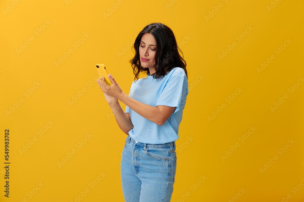 Woman blogger with a phone in her hands in a blue t-shirt and jeans on a  yellow background smile signs gestures symbols, online communication and  video call, copy space, free background Stock