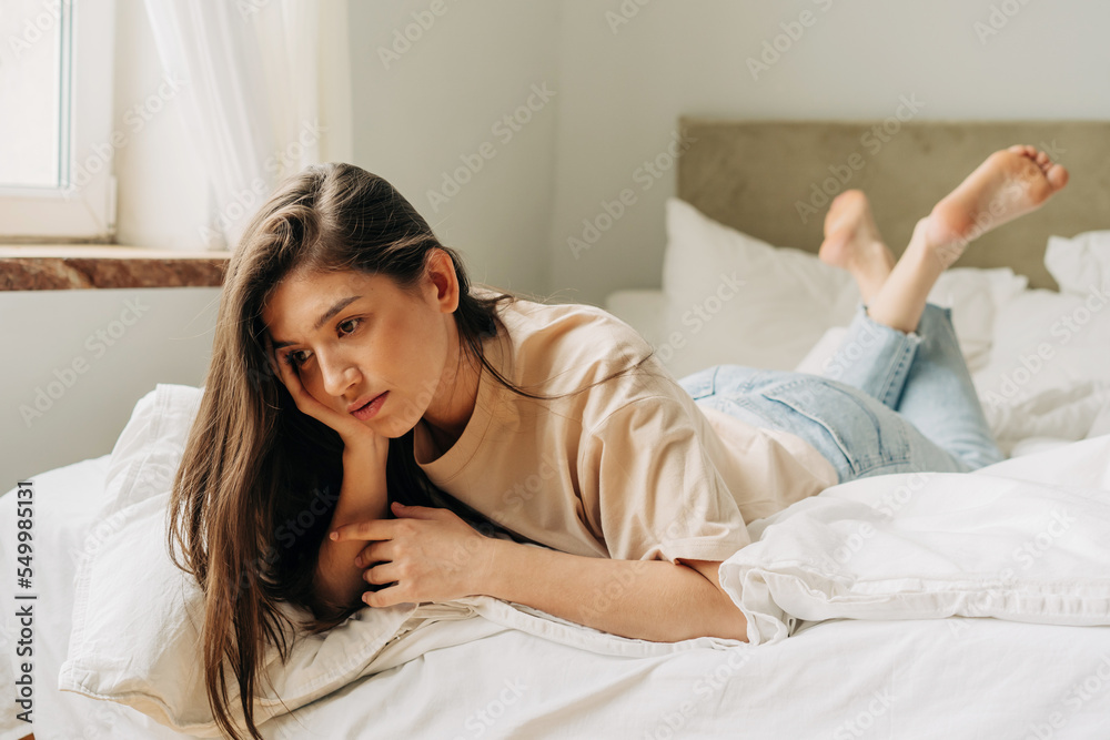 Sad lonely bored pensive girl lies on the bed