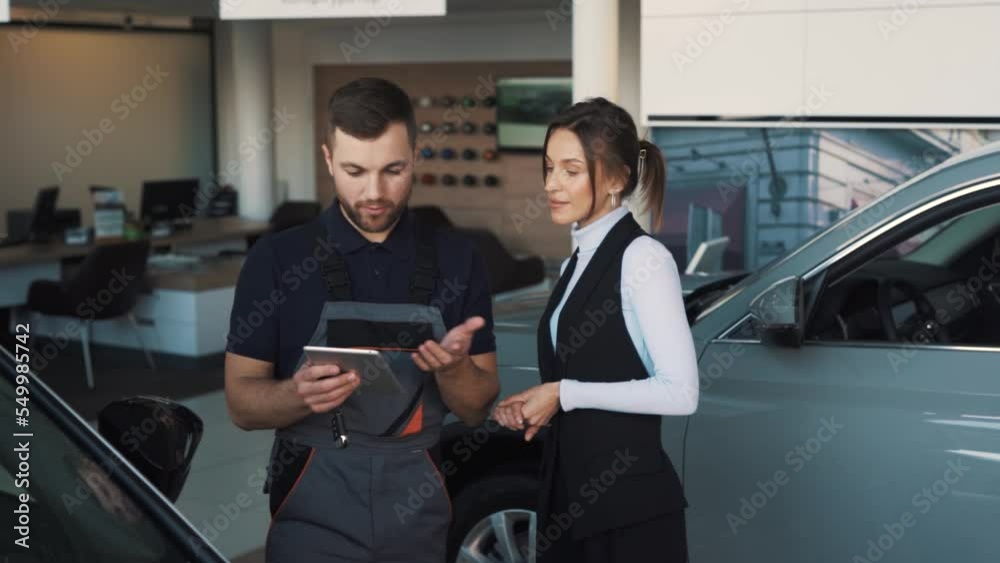 a stylish car mechanic gives a sign in a tablet and gives the keys to a young woman car owner