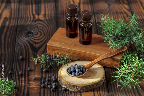 Fresh purple organic juniper berries in a wooden spoon and a bottle of oil on a wooden background