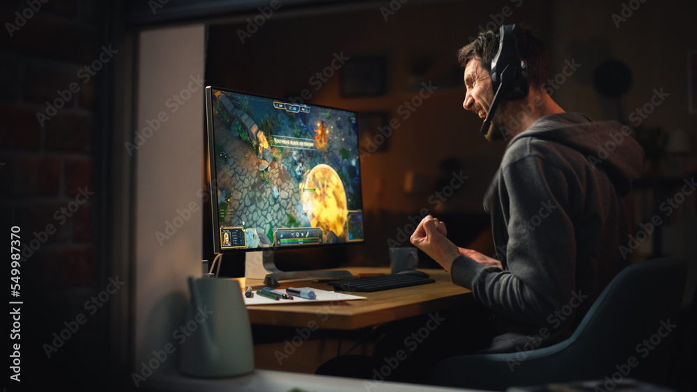 Excited Middle Aged Male Gamer Playing Online Video Game on Personal Computer. Guy Enjoying Fantasy RPG Game with Role Playing Character Casting Spells, Destroy Enemies. Shot from Outdoors.