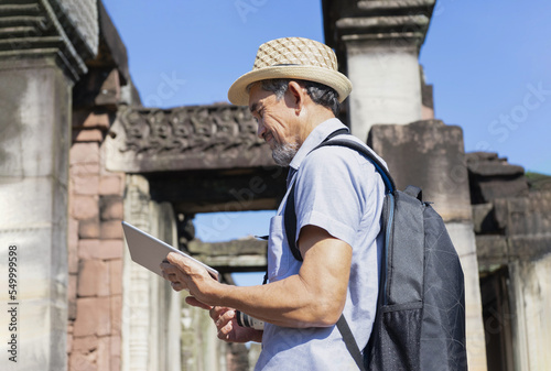 senior man wearing hat with backpack, camera and tablet computer in hand is searching data at ancient archaeological site.concept tourism ancient sites, archaeologist, archeology work © Verin