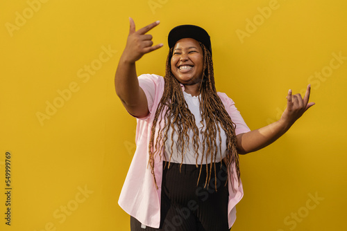 Happy woman showing horn sign gesture in front of yellow wall