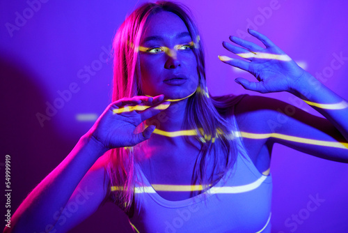 Woman gesturing with neon colored lighting in front of wall