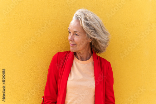 Thoughtful mature woman in front of yellow wall photo