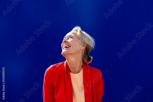 Happy woman with red blazer in front of blue wall