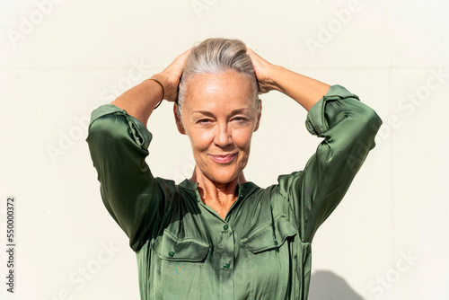 Confident woman with hands behind head in front of white wall photo