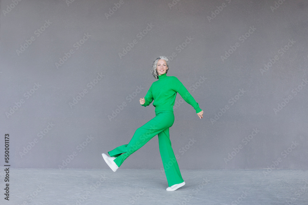 Smiling woman standing on one leg in front of gray wall Smiling woman standing on one leg in front of gray wall
