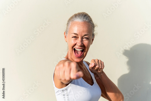 Happy woman showing fists in front of wall on sunny day photo