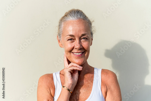 Smiling mature woman with hand on chin in front of cream colored wall