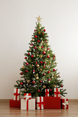 Big beautiful christmas tree decorated with shiny baubles and many different presents on wooden floor. White wall background with a lot of copy space for text. Close up.