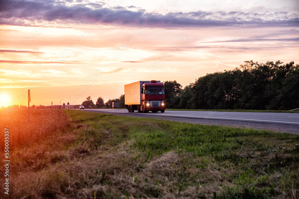 Fototapeta premium A modern truck with a semitrailer refrigerator transports cargo against the backdrop of an evening sunset in summer. Road freight industry. Goods turnover,