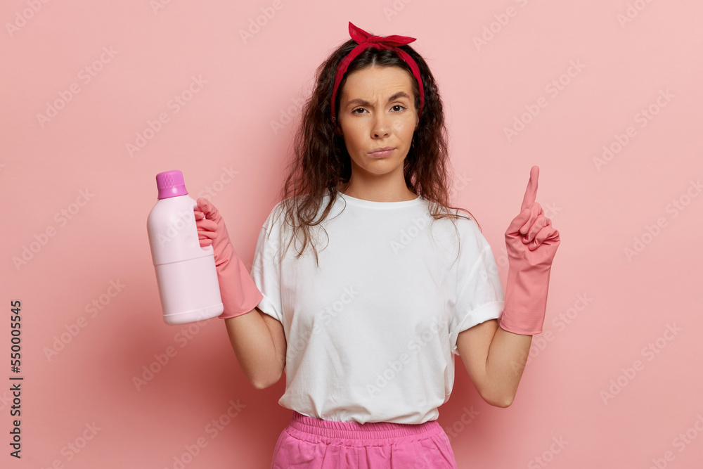 pretty housewife stands next to the pink wall, holds liquid for cleaning pretty housewife stands next to the pink wall, holds liquid for cleaning