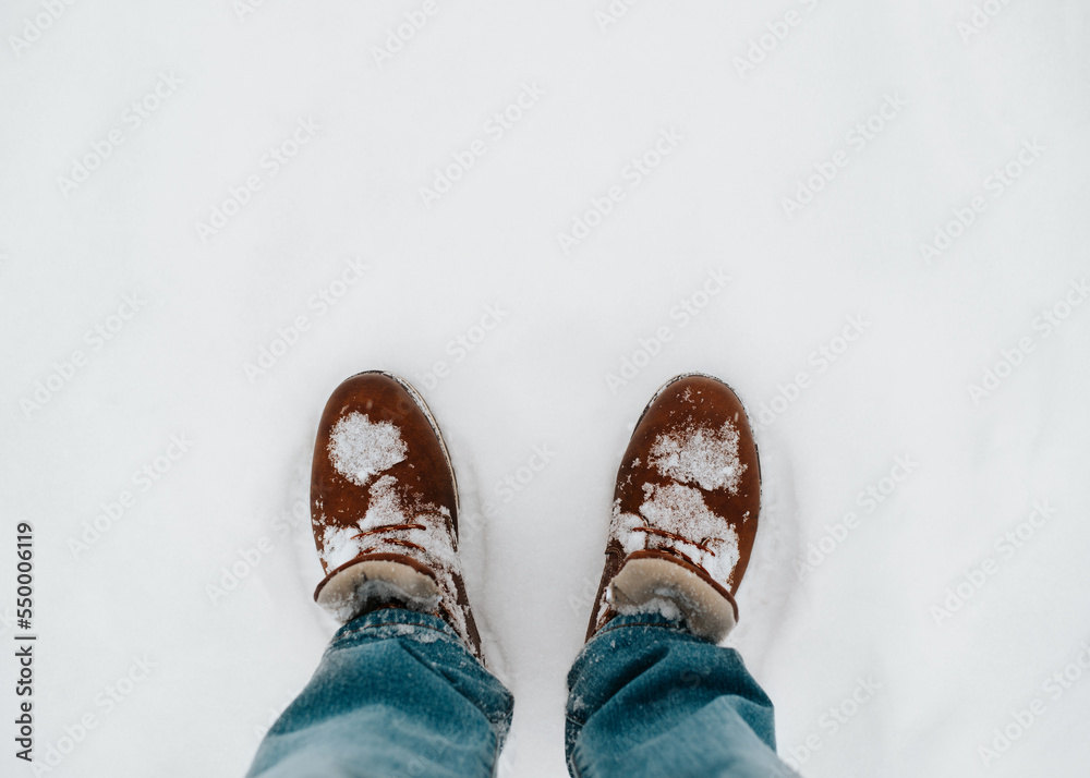 Man wearing winter leather brown boots and blue jeans standing in snow outdoors. Top view, close-up, copy space Man wearing winter leather brown boots and blue jeans standing in snow outdoors. Top view, close-up, copy space