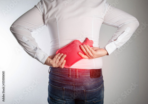 A man holds a medical heating pad with hot water in the lumbar spine. Relaxation of the back muscles with back pain, lumbago. Pinched nerve, close-up