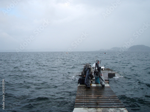 Wooden pier and fishing tackle sticking out into the rough sea during the rain. photo
