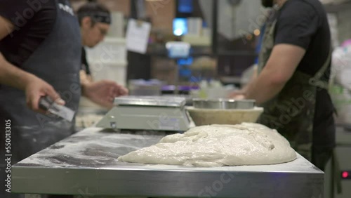 tattooed baker kneading bread doughs and placing the doughs with flour on the workbench of the bread workshop